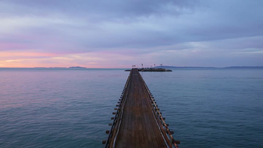 A pier stretches across the water as the colors of the sky are reflected in the water as it ripples
