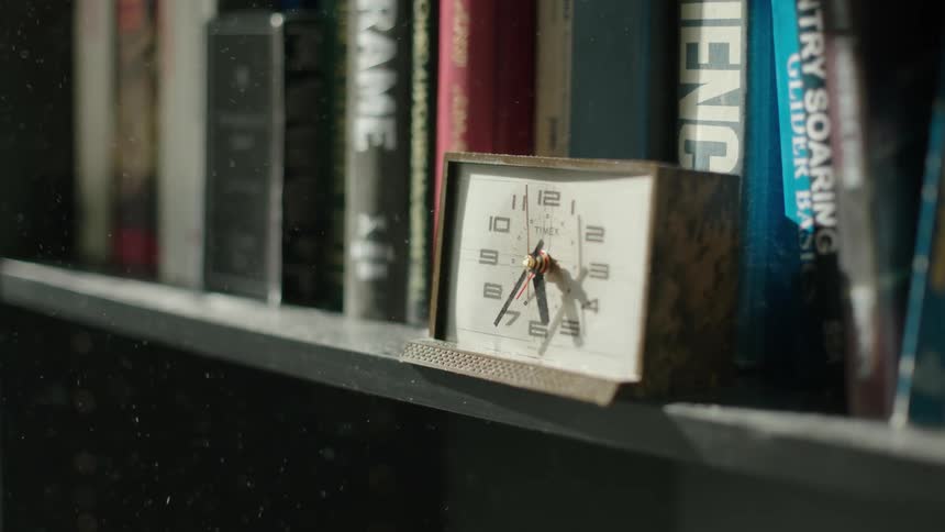 A analog clock sits on a shelf filled with books