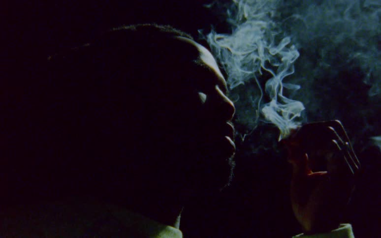 Man with dreadlocks and beard smokes a cigarette in the dark