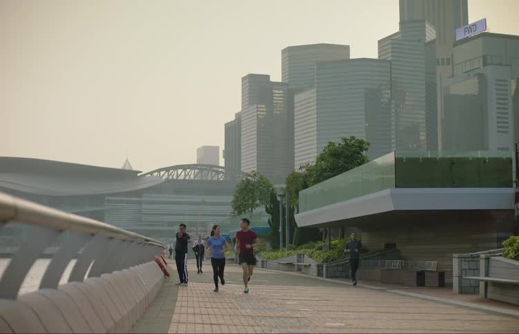 Asian man and asian woman jogging and talking together at a public space in a big city with tall buildings at a distance