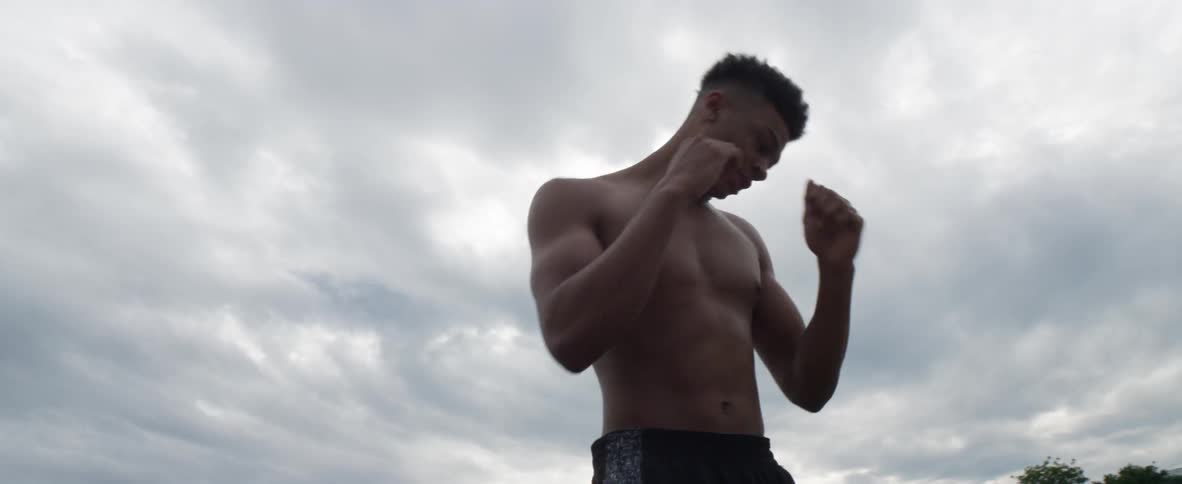 Shirtless young black man practicing boxing punches outdoors