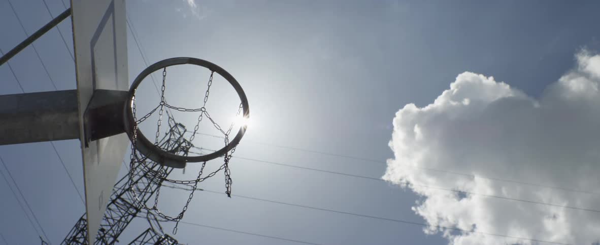 View of a basketball hoop from below in a sunny day with clouds in the sky