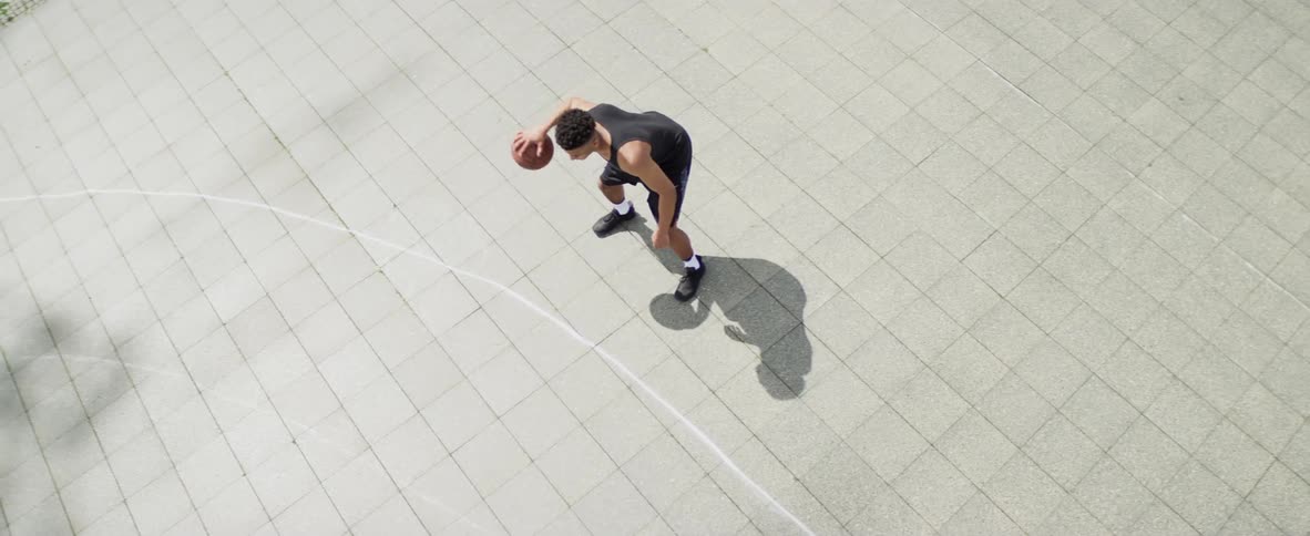 A man dribbles a basketball while standing at an outdoor court