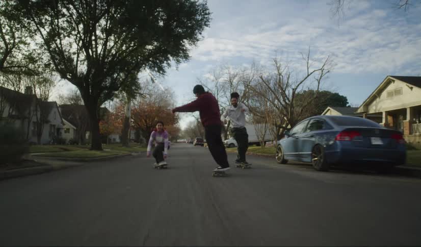 Three young people are skating on a neighborhood street