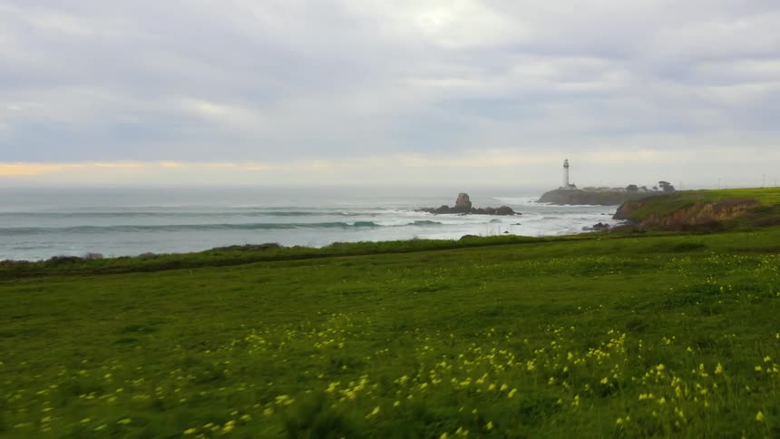 Waves splash over rocks along the coastline and a lighthouse is overlooking the water