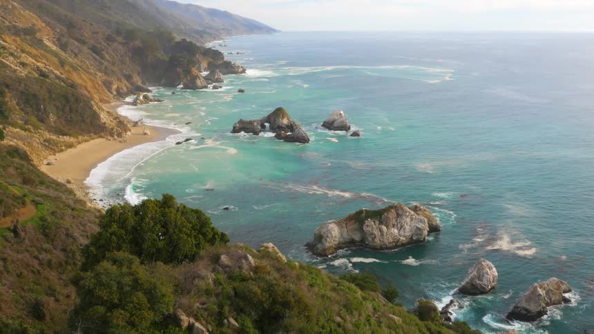 Aerial view of the coastline as waves splash against the rocks and roll in over the beach
