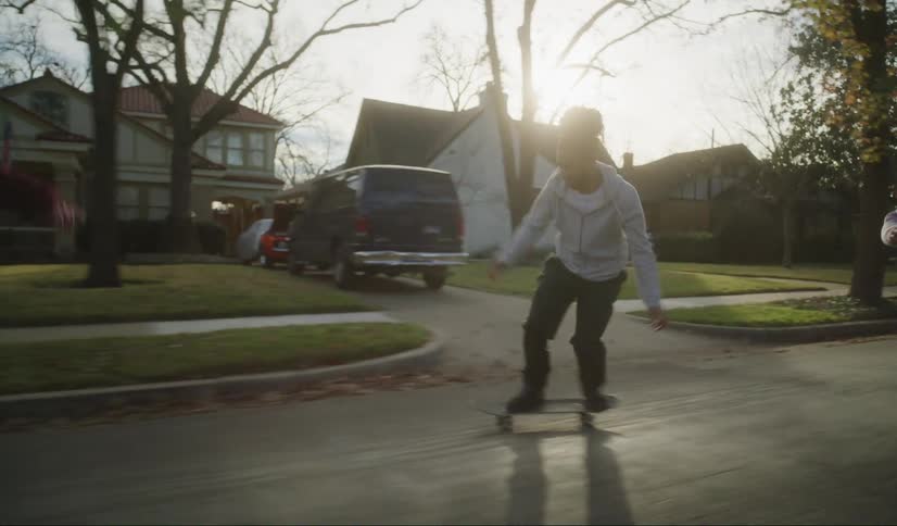 A group of skateboarders skate along a road through a neighborhood during the day