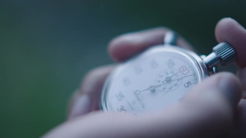 A person holds and clicks the switch on an analog stopwatch