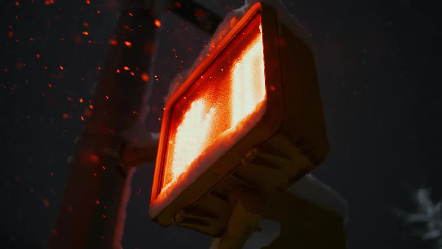 Snow is falling onto a crossing signal sign at night