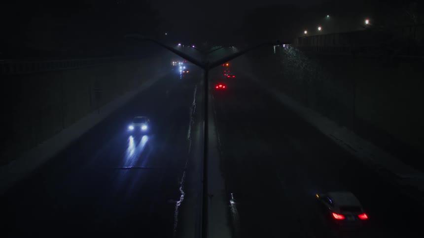 Headlights and tail lights shine and reflect on the road as traffic moves on a freeway in the snow at night