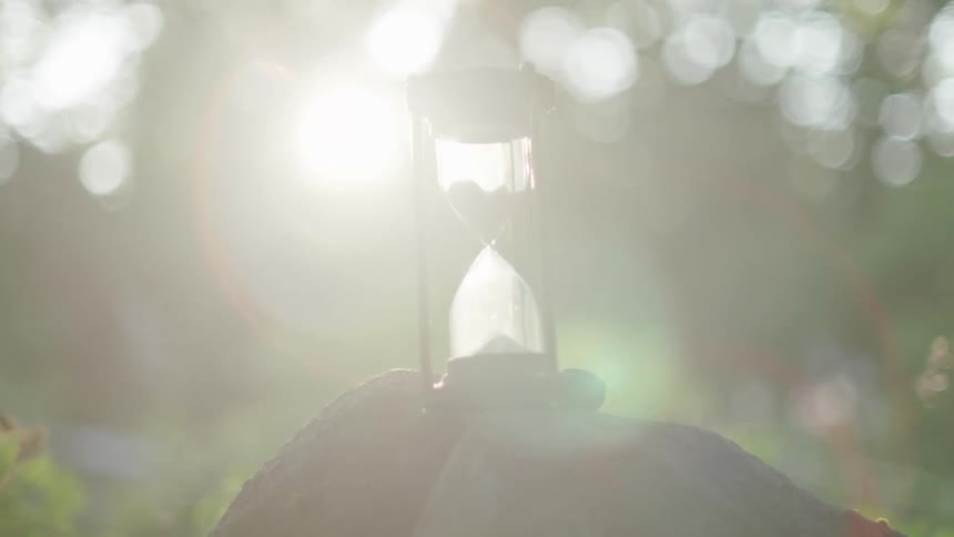 The sun shines brightly upon an hourglass sitting on a rock