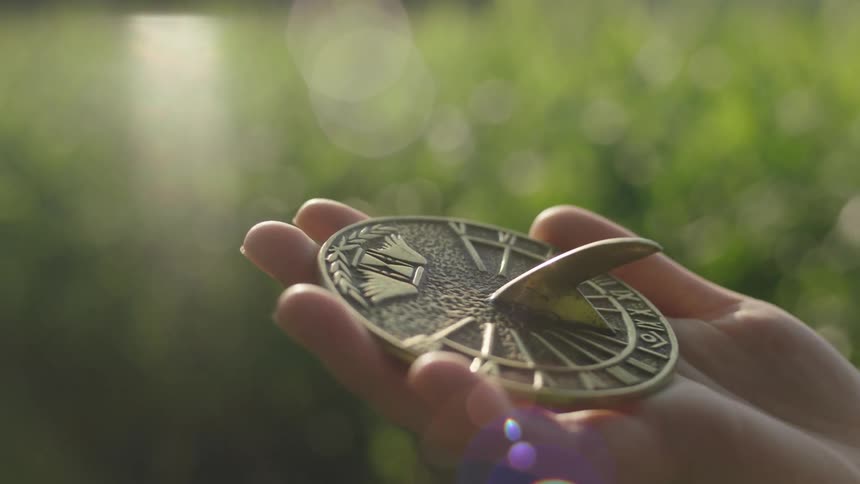 The sun shines brightly on a girls hand holding a sun dial