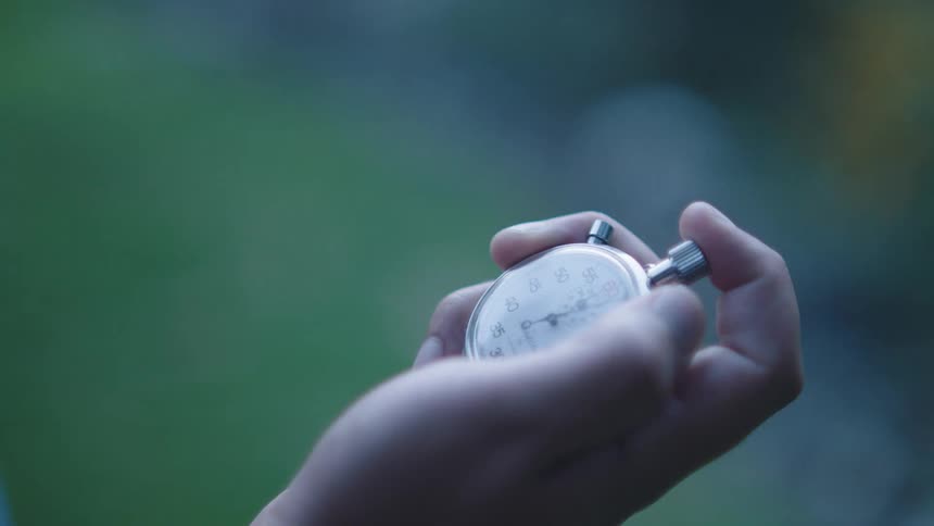 White man standing outdoors holding a stopwatch and pressing the start button