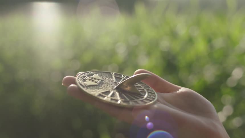 A woman holds up a compass style sundial while standing in a field