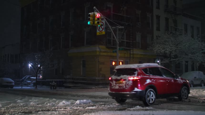 A pedestrian crosses snow covered street as vehicles move through nearby intersection