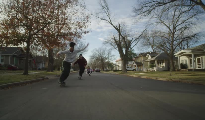 Three teens ride skateboards down the middle of a neighborhood street