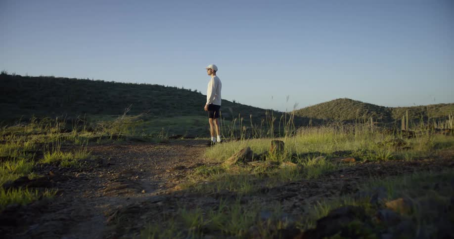 A man is standing on a grassy hilltop and looking out over a landscape in the afternoon