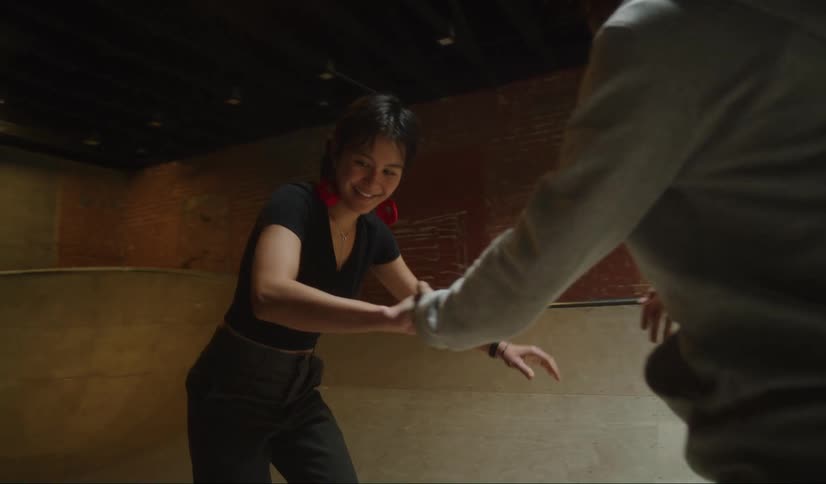Man helps woman learn to skateboard back and forth in skatepark bowl