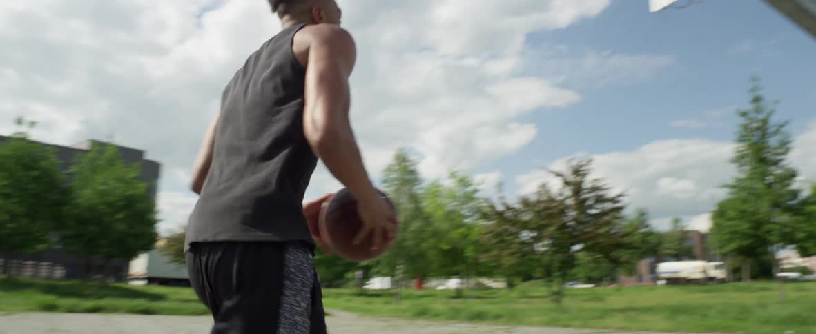 A man dribbles a basketball and shoots for a basket at an outdoor court