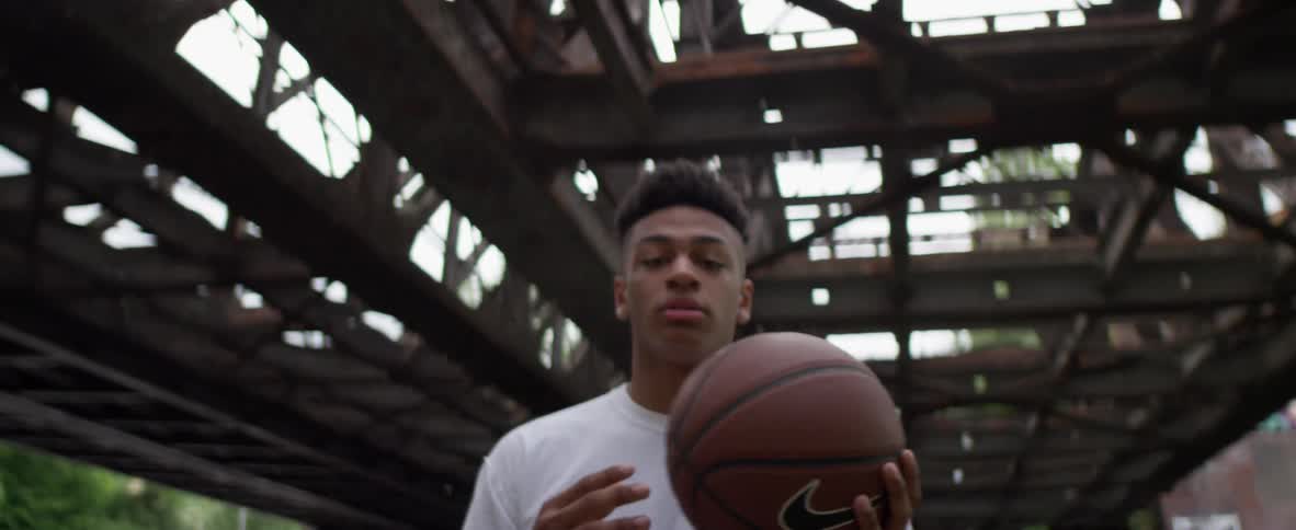 A man tosses a basketball from hand to hand while standing outside under steel beams