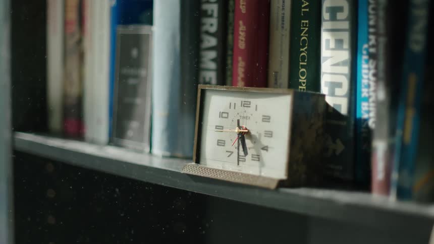 A vintage alarm clock sitting on a book shelf as dust particles fall