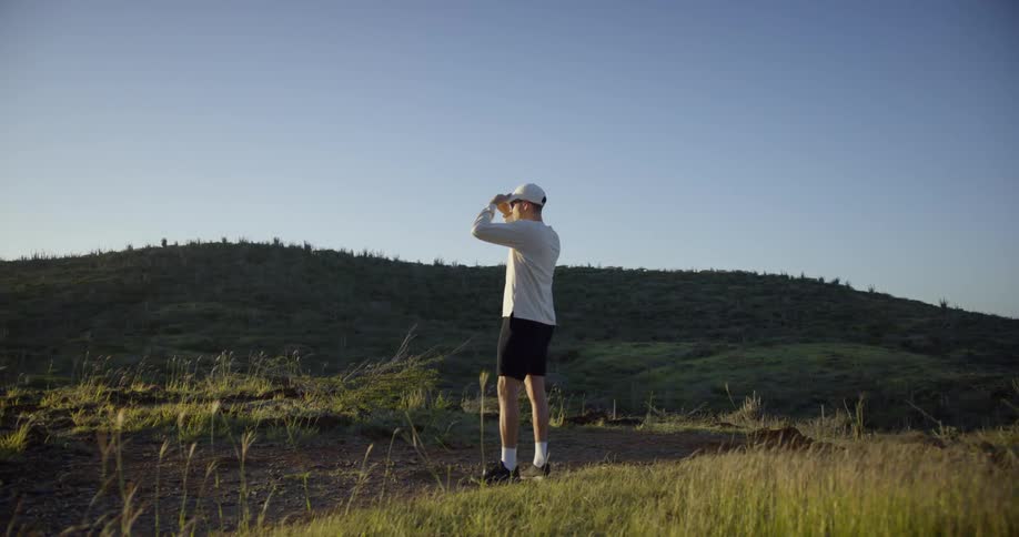 A man standing on a dirt trail in the hills looking out in the distance
