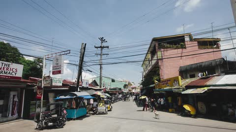 Traffic flows by businesses on a city street with electrical wires hanging overhead