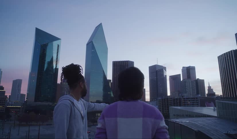A man and woman stand on a rooftop and look at the city skyline
