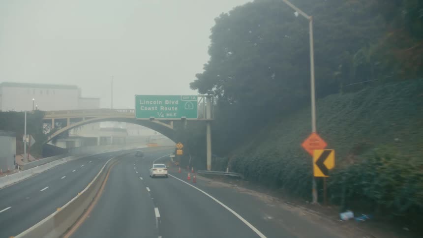 Automobiles travel through a dark tunnel and into the foggy daylight on a freeway