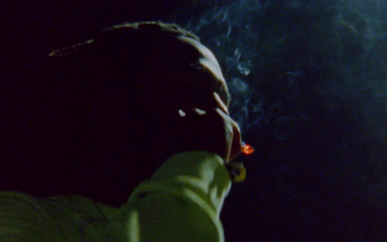 Man with dreadlocks and beard smokes a cigarette in the dark