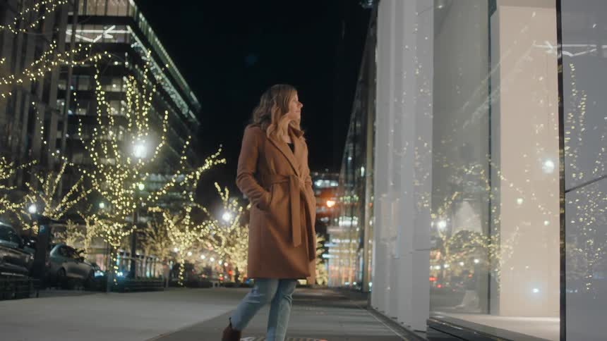 A woman walks on the pathway and stops next to a store window and looks inside