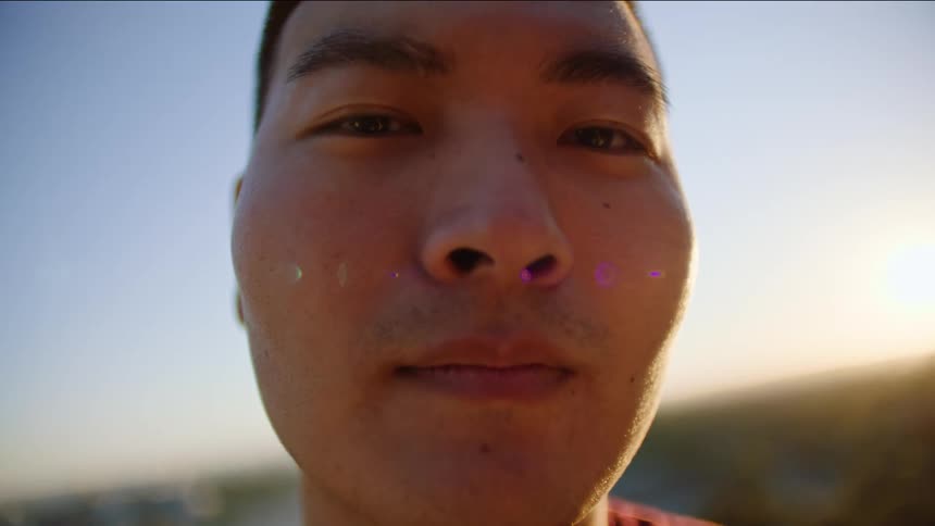 Face of a young asian man standing outdoors at a sunny day