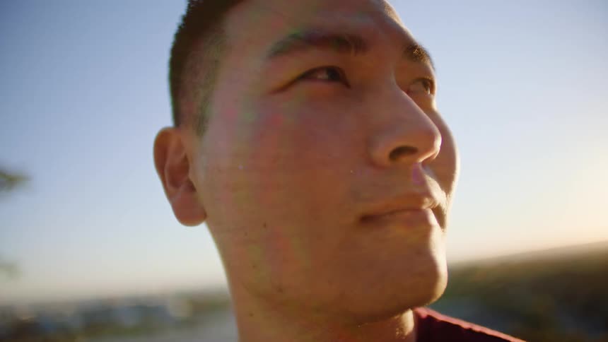 A young asian man stares off into the distance from atop a mountain