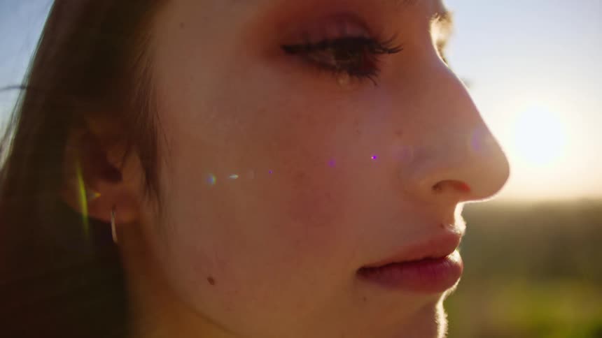 A tear runs down a womans face as she stands in a field
