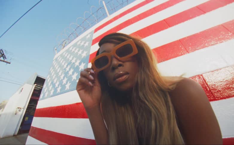 Young black woman wearing sunglasses standing in the front of an american flag painted wall