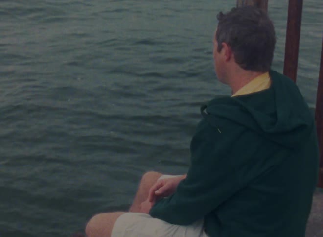 A man stands with his legs dangling above a lake