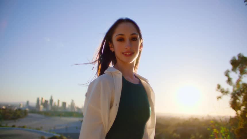 Woman with long hair white and black shirt looks at camera smiling at sunset