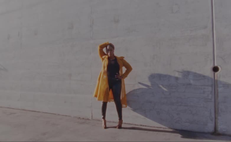 Woman with dreadlocks yellow jacket black shirt pants and high heels poses for camera