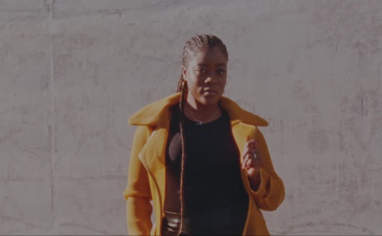 A woman unzips her puffer coat while posing in front of a concrete wall