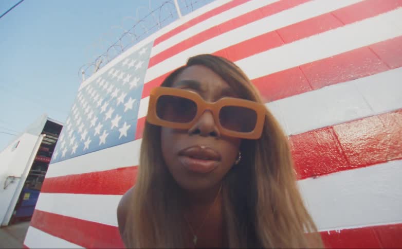A women moves her head forward and back while standing in front of a wall painted like an american flag