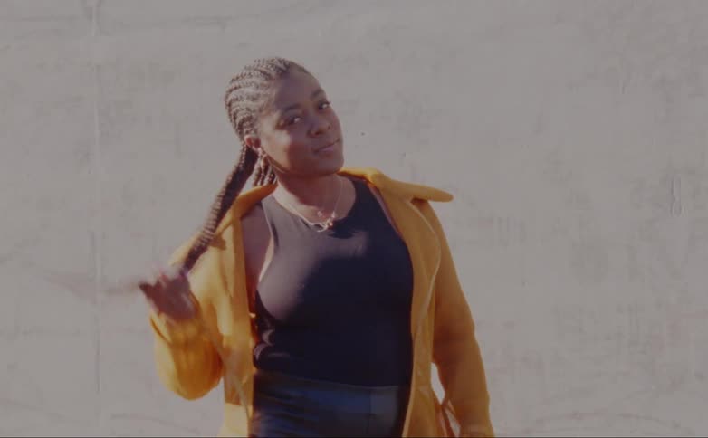 Female model with dreadlocks hoop earrings yellow overcoat and black shirt poses for the camera