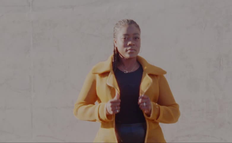 Female model with dreadlocks hoop earrings yellow overcoat and black shirt poses for the camera