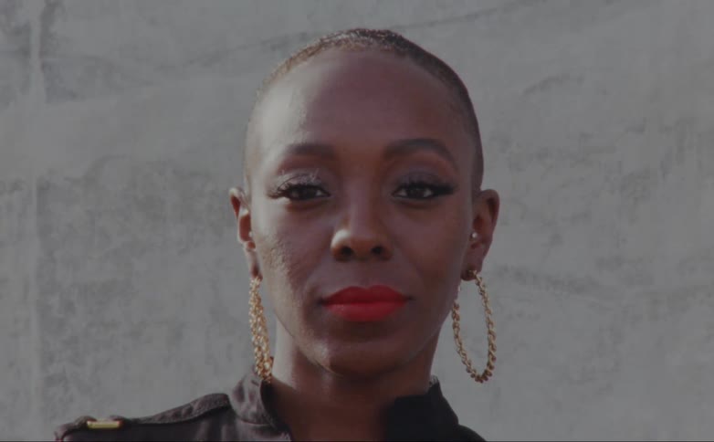 A woman is standing outside while staring into the camera