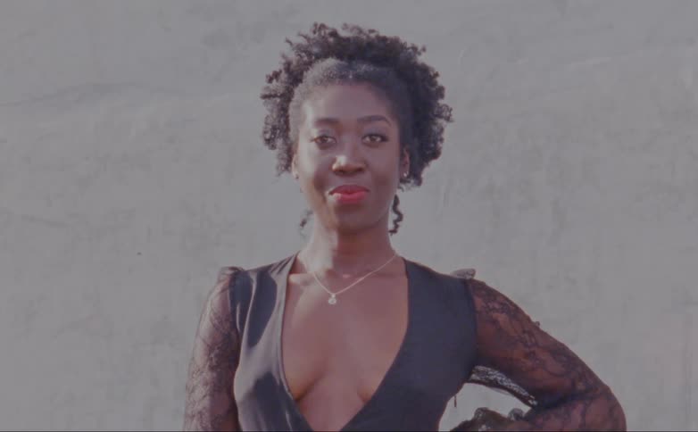 Woman with curly hair and black plunging gown faces the camera with eye contact