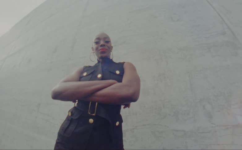 A woman crosses her arms as she poses in front of a concrete wall