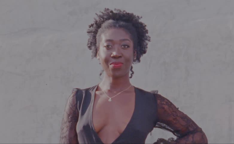 A woman is standing outside in the daytime while posing in front of a camera