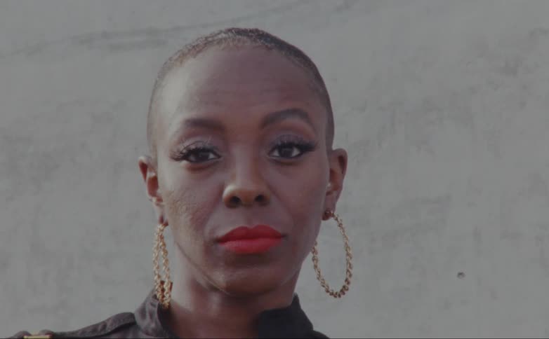 A woman raises her eyebrow while posing in front of a wall outside