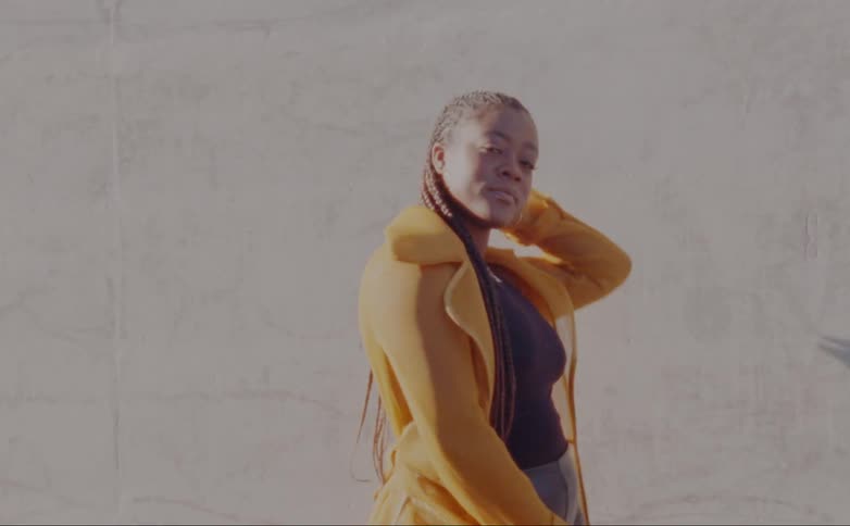 Woman with dreadlocks hoop earrings yellow jacket and black shirt poses for the camera