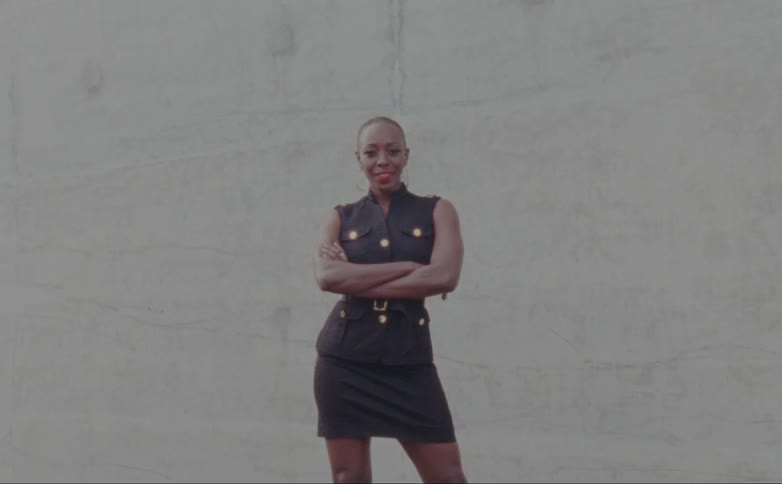 Bald female model with hoop earrings and short black dress stands with her arms crossed posing for the camera