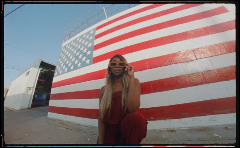 A woman is kneeling and posing in front of a building with an american flag mural in the daytime